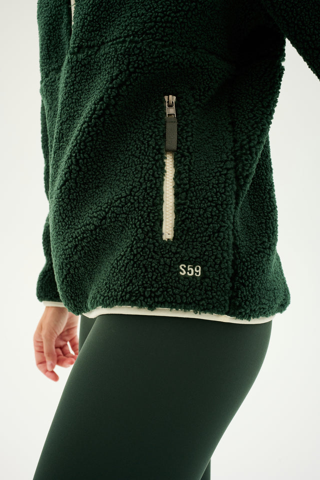 Close-up of a person wearing a Libby Sherpa Half Zip in Military/Creme by SPLITS59, paired with matching leggings—perfect for warming up during winter workouts.