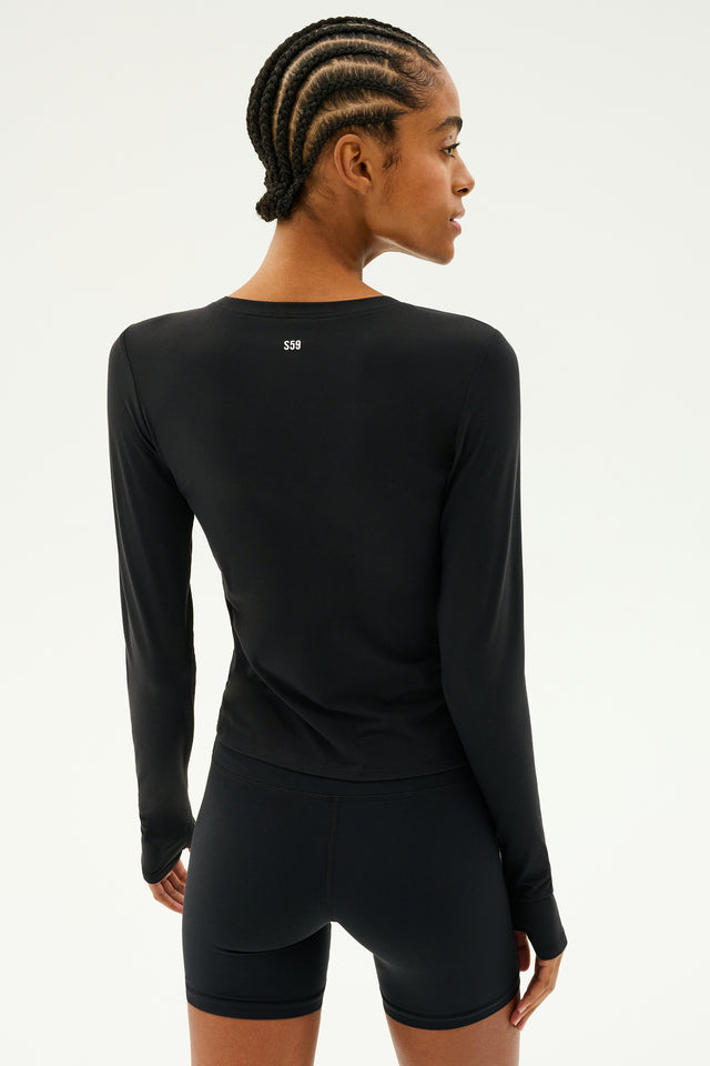 A person with cornrows is wearing the SPLITS59 Airweight Lite LS Waist Length top in black, paired with shorts, standing facing away and possibly gearing up for a workout.