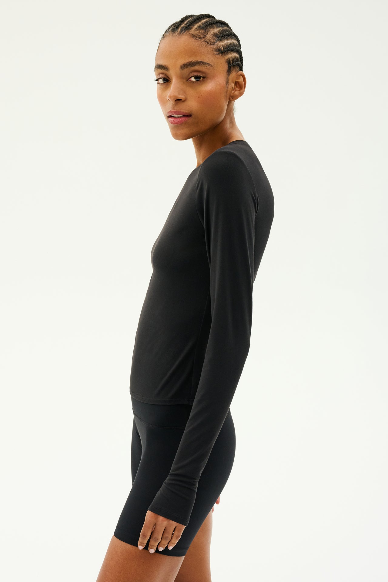 Person wearing a black Airweight Lite long-sleeve waist-length top from SPLITS59 and shorts, looking over their shoulder against a plain background, ready for gym workouts.