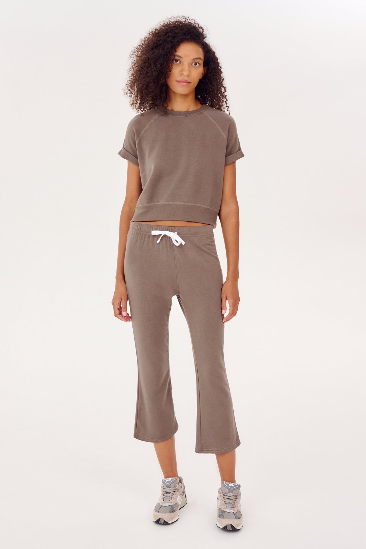 The model is wearing cozy SPLITS59 Lentil Brooks Fleece Cropped Flare sweatpants and a tan crop top.