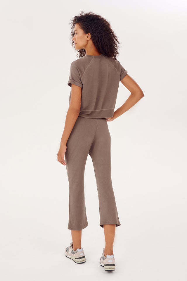 The back view of a woman wearing SPLITS59 Brooks Fleece Cropped Flare - Lentil pants and sneakers.