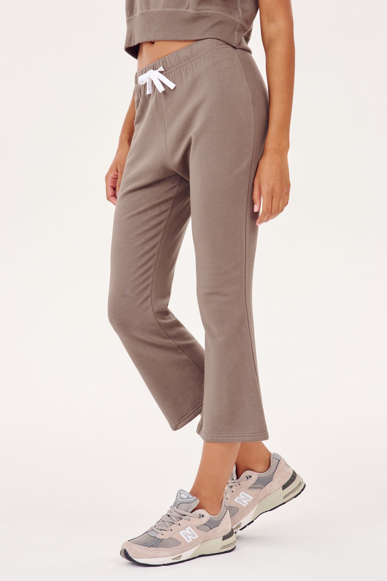 A woman wearing cozy, tan Brooks Fleece Cropped Flare - Lentil sweat pants and sneakers, ideal for workouts from SPLITS59.
