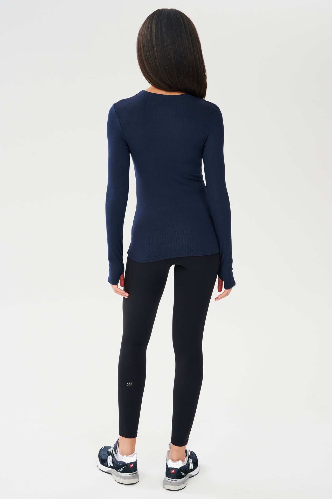 The back view of a woman wearing a SPLITS59 Louise Rib Long Sleeve in Indigo and black leggings, ready for her yoga session.