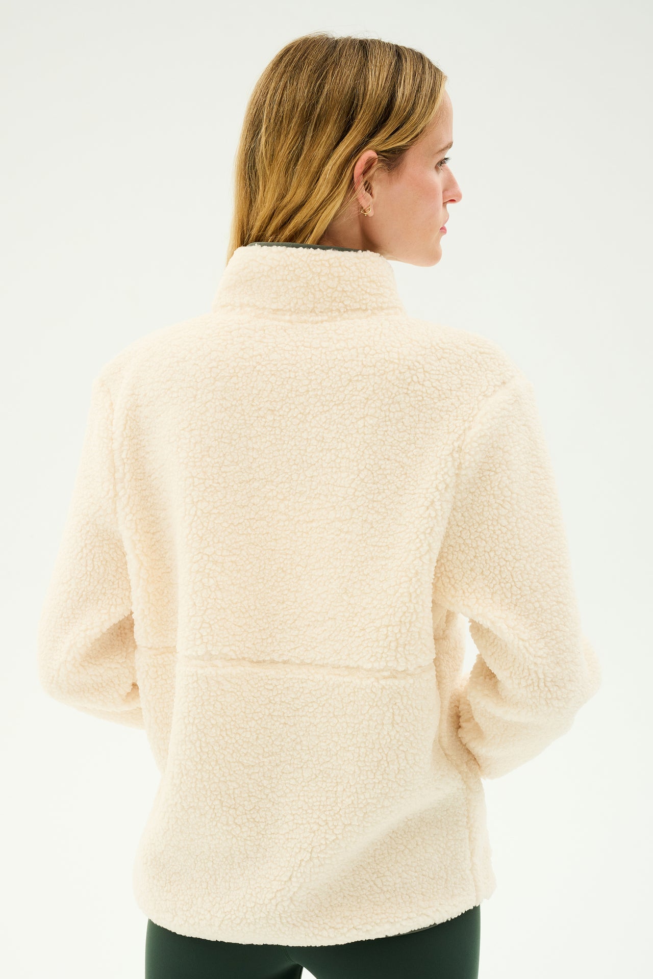 A woman with long blonde hair is wearing the SPLITS59 Libby Sherpa Half Zip in Creme/Military, viewed from the back. She is standing in front of a plain white background.