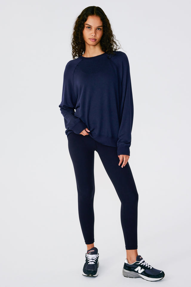 Full front view of girl wearing dark blue sweatshirt with visible stitching and ribbed hem with dark blue leggings and dark blue shoes