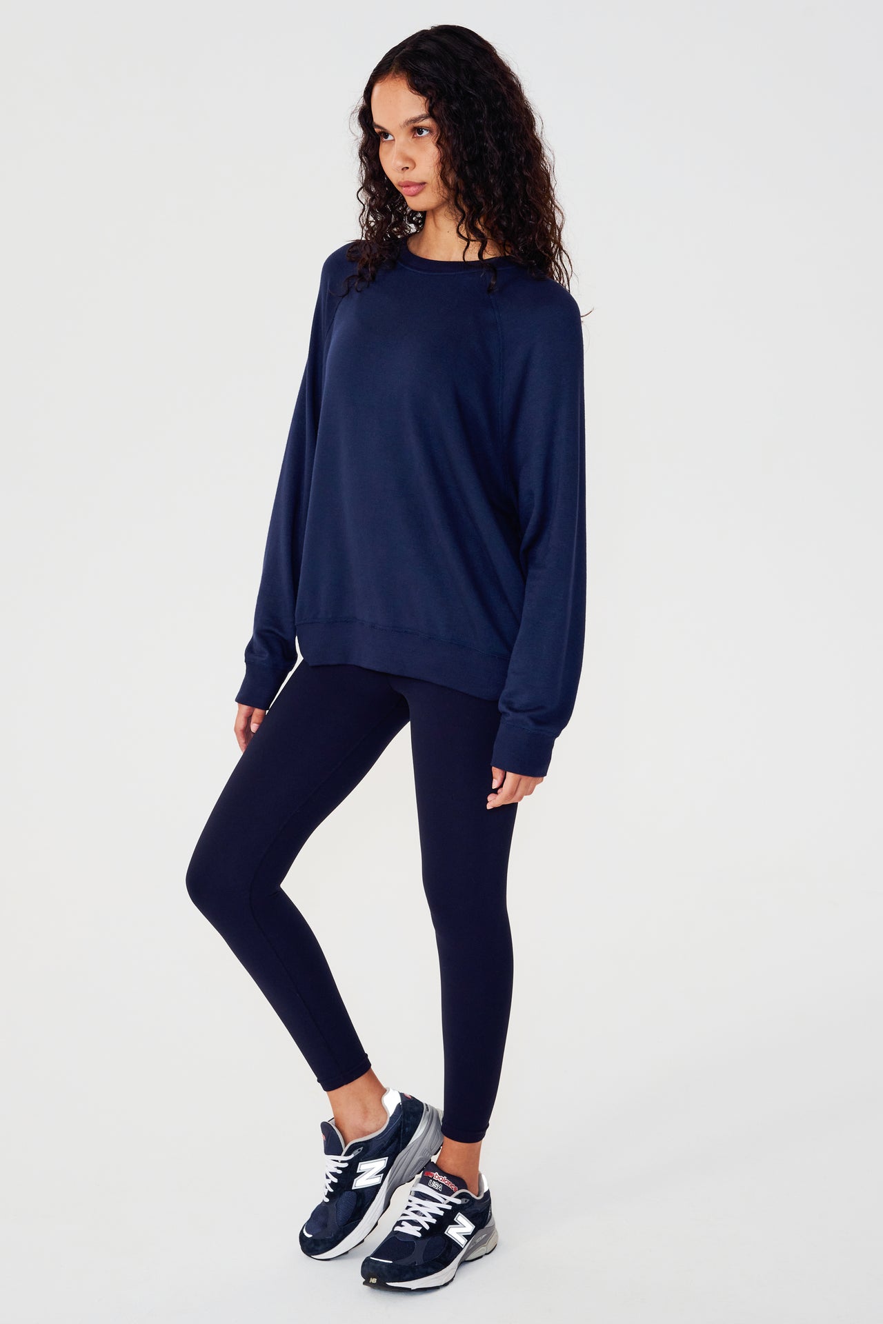 Full side view of girl wearing dark blue sweatshirt with visible stitching and ribbed hem, with dark blue leggings and dark blue shoes
