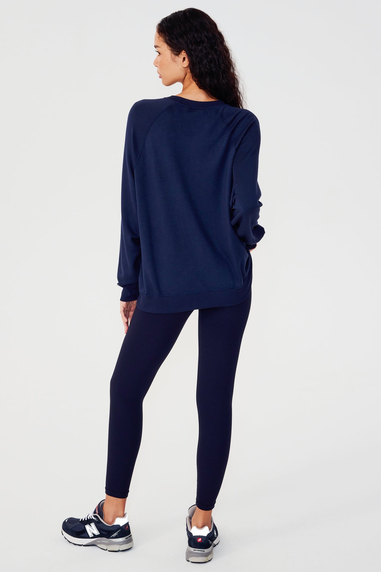 Full back view of girl wearing dark blue sweatshirt with visible stitching and ribbed hem with dark blue leggings and dark blue shoes