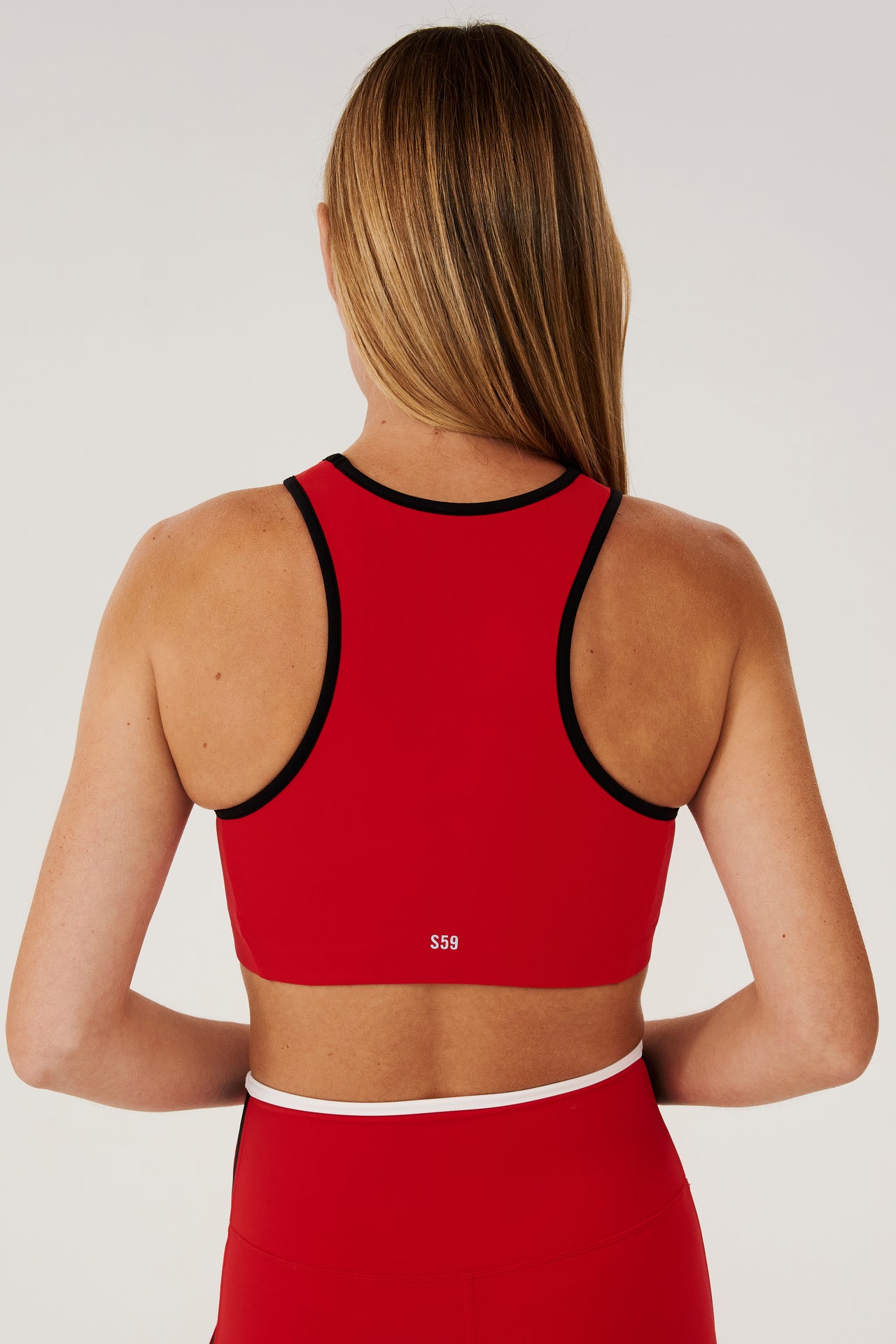 Back view of girl wearing red sports bra with black hem and red leggings with white stripe around the waistband 