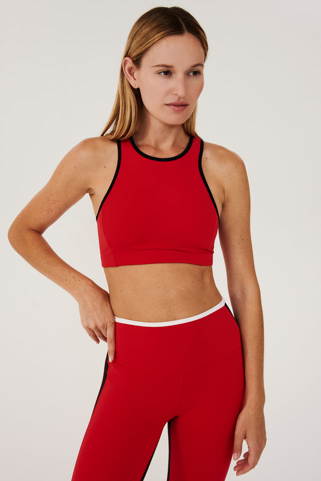 Front view of girl wearing red sports bra with black hem and red leggings with white stripe around the waistband and black stripe down the outer seam and a black stripe on inseam 