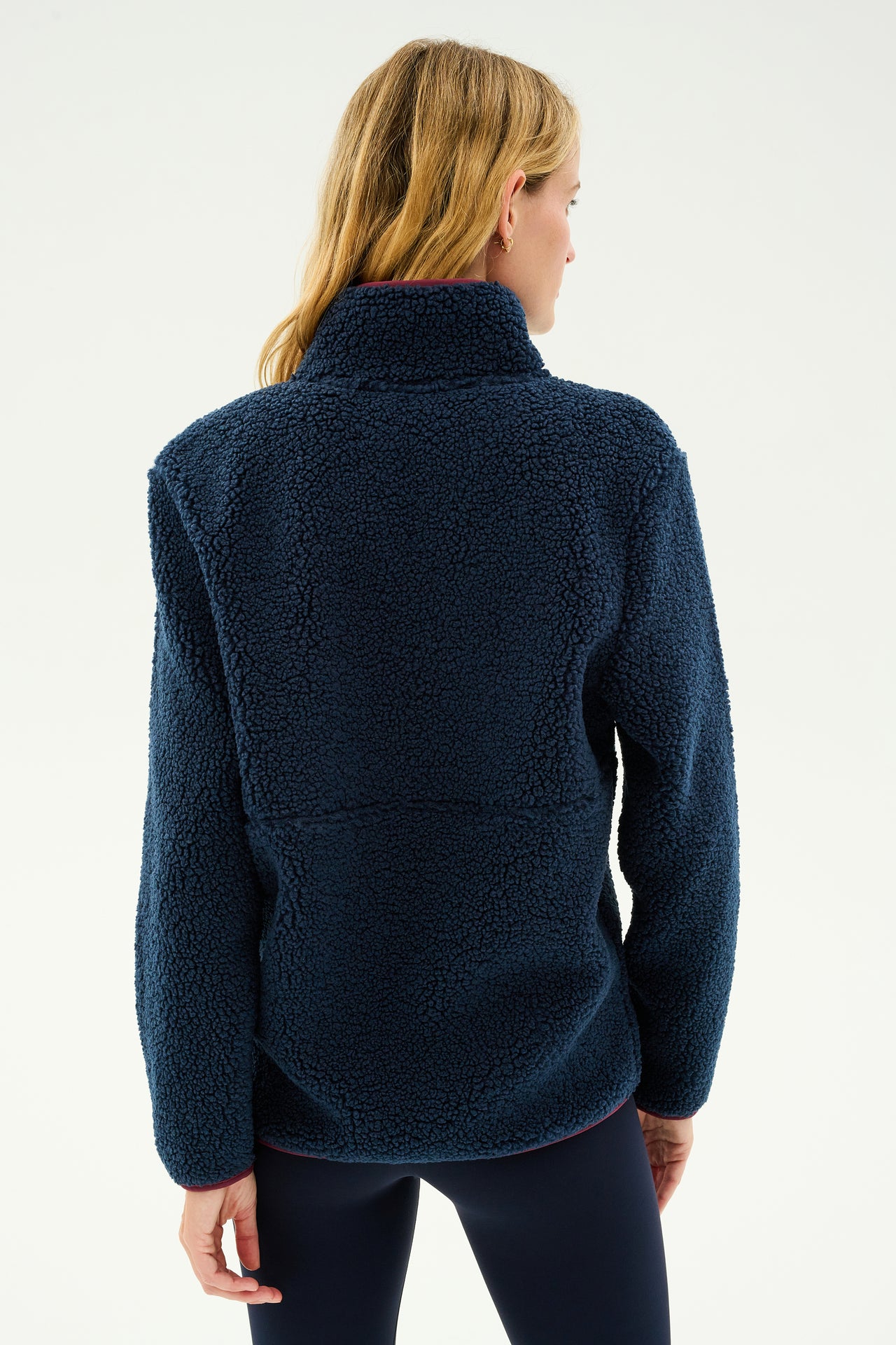 A woman with long blonde hair is seen from the back, wearing the SPLITS59 Libby Sherpa Half Zip in Indigo/Dark Cherry, perfect for winter workouts.