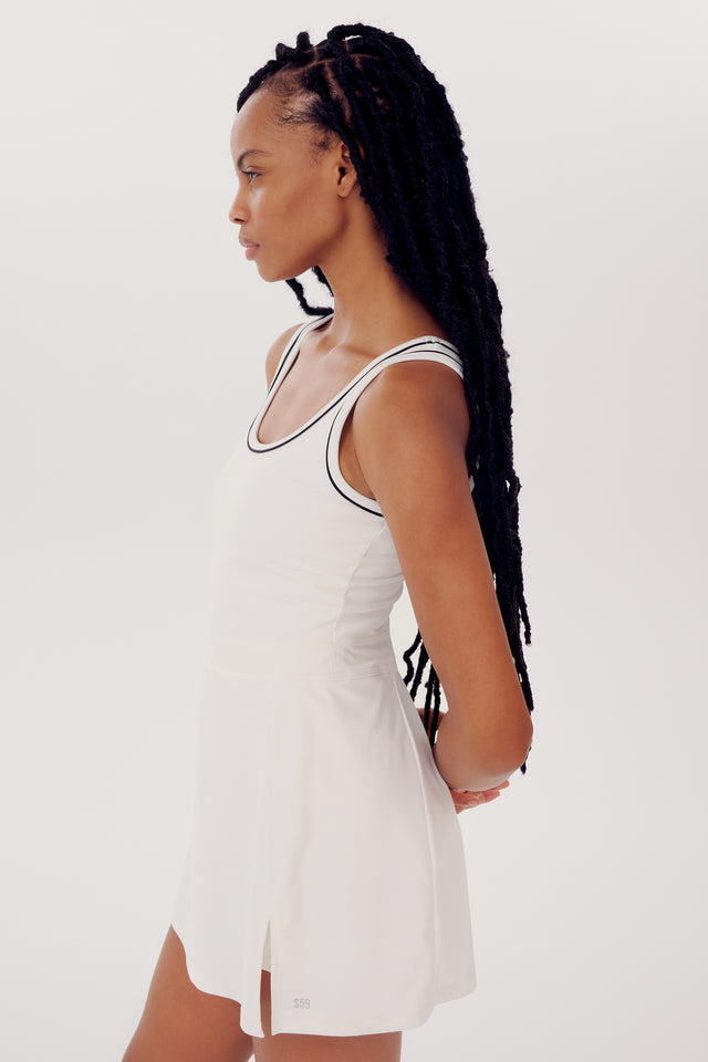 A young woman with long braids wearing a white SPLITS59 Martina Rigor Dress W/Piping, standing in profile against a plain background.