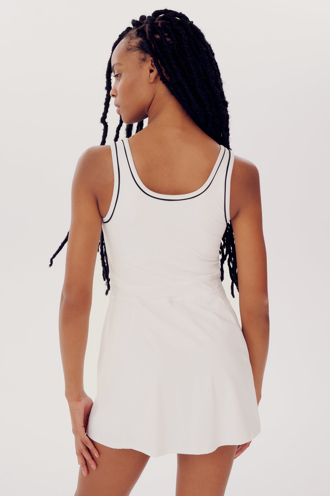 Person with long braided hair wearing a sleeveless white Martina Rigor Dress w/Piping - White by SPLITS59, facing away from the camera.