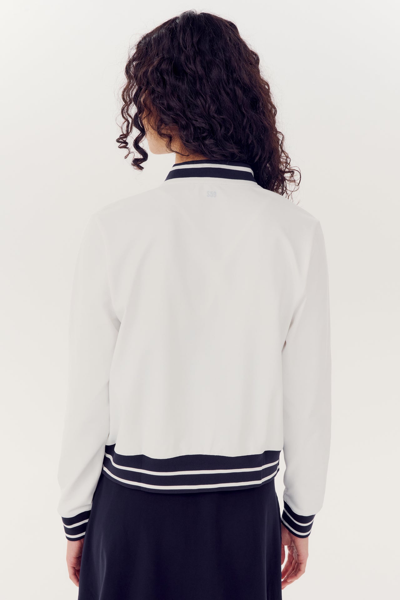 Woman viewed from behind, wearing a white SPLITS59 Ever Supplex Jacket with black and white striped cuffs and collar.