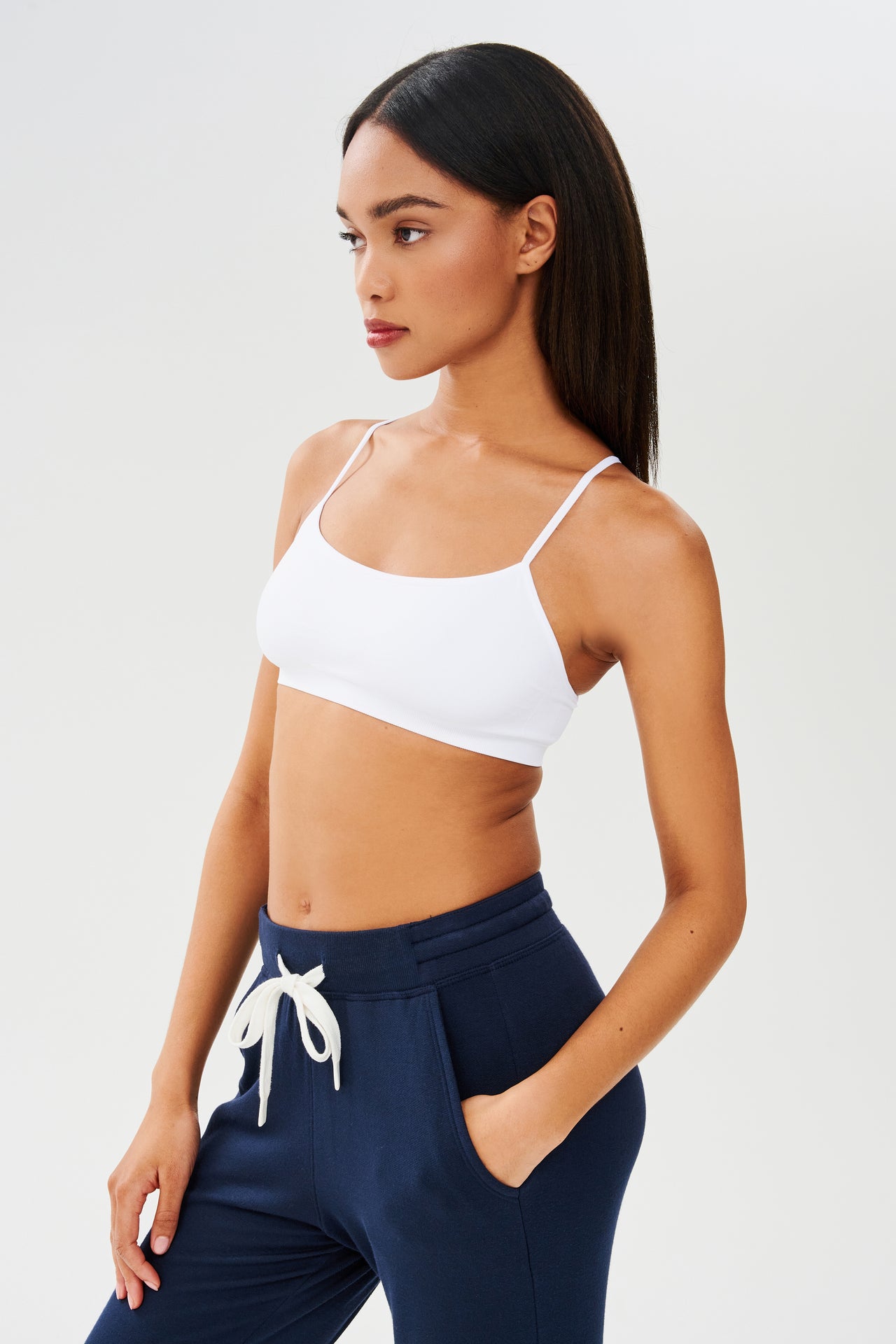 The model is wearing a Splits59 Loren Seamless Bra in White and navy sweatpants, perfect for chafe-free gym workouts.