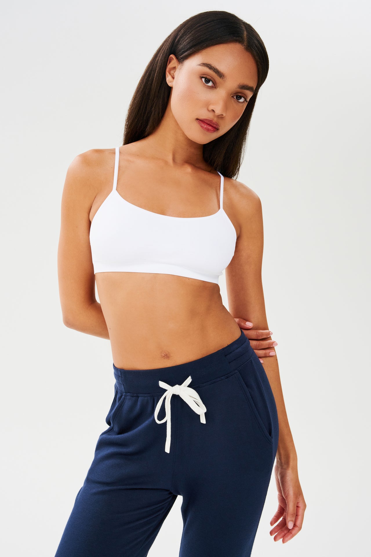 The model is wearing a Splits59 Loren Seamless Bra in White and navy sweatpants, perfect for gym workouts.