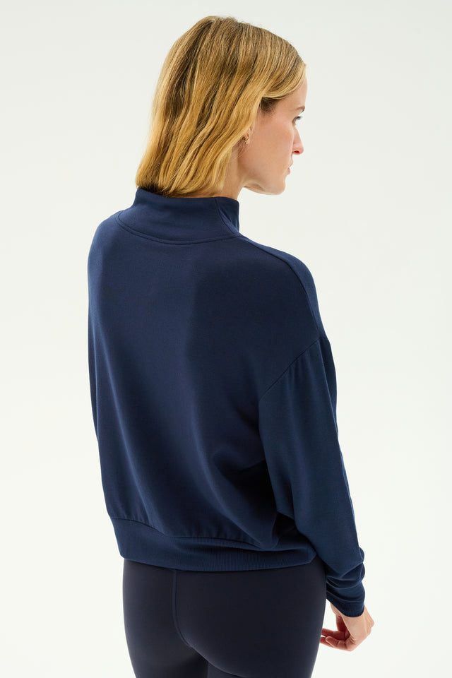 Person wearing an indigo Birdie Fleece Half Zip from SPLITS59 and black leggings, viewed from behind, perfect for winter workouts with its cozy stretch modal fabric.