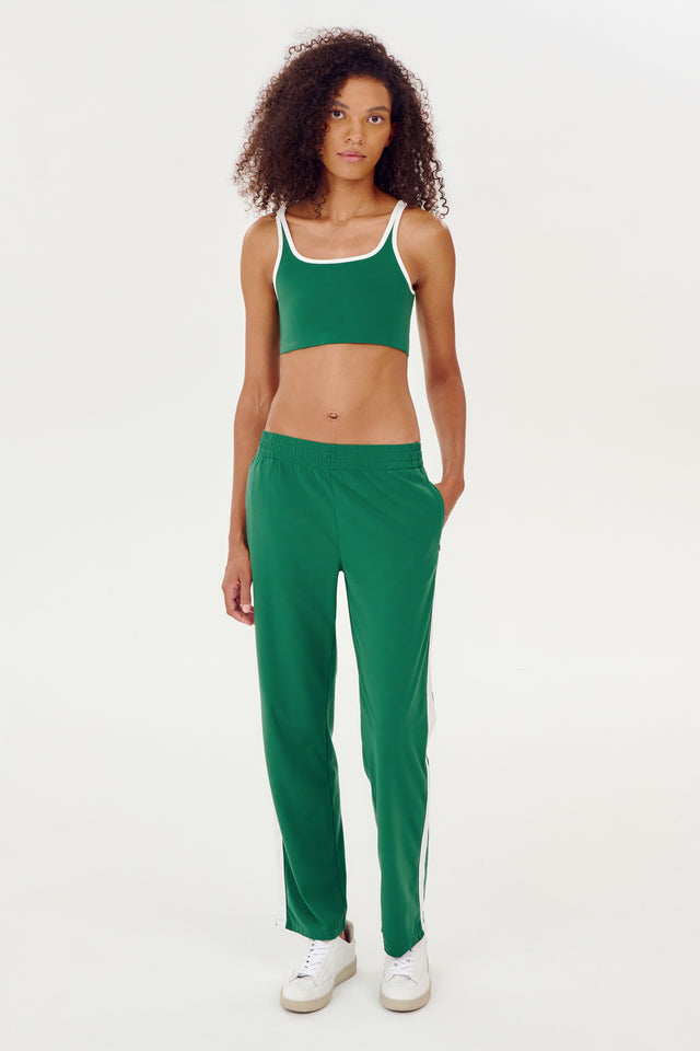 A woman wearing SPLITS59's Max Rigor Track Pant in Arugula/White and a white crop top engages in outdoor workouts.