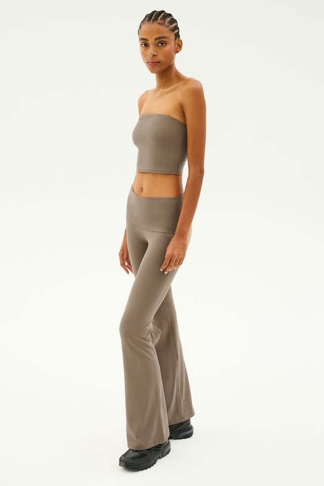 A person wearing a Hazel Airweight Crop Bandeau in Lentil by SPLITS59 and bell-bottom pants made of stretch fabric, paired with black shoes, stands against a white background.