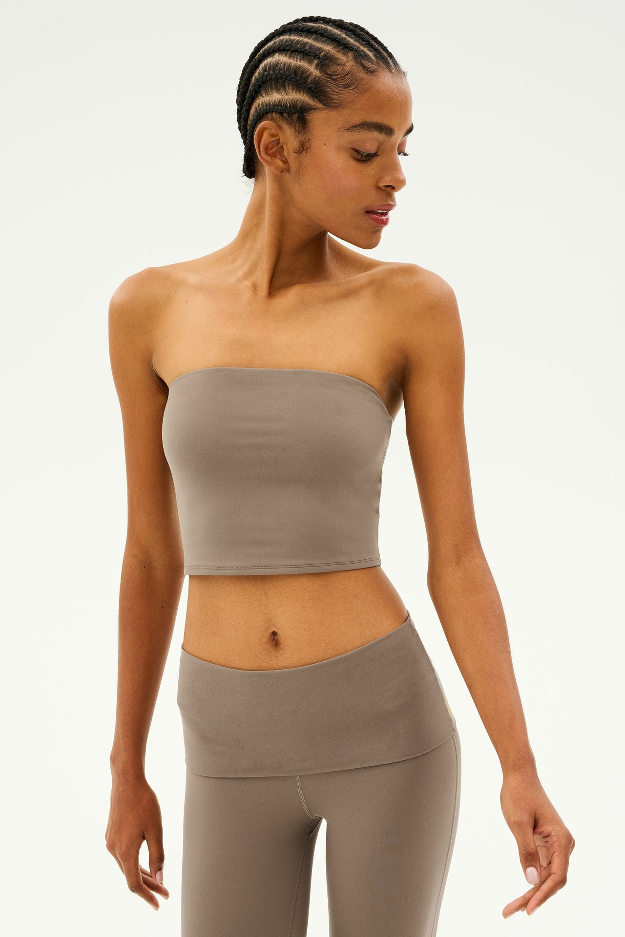 A person wearing the Hazel Airweight Crop Bandeau in lentil color from SPLITS59, paired with stretch fabric leggings, gazes gracefully downward.