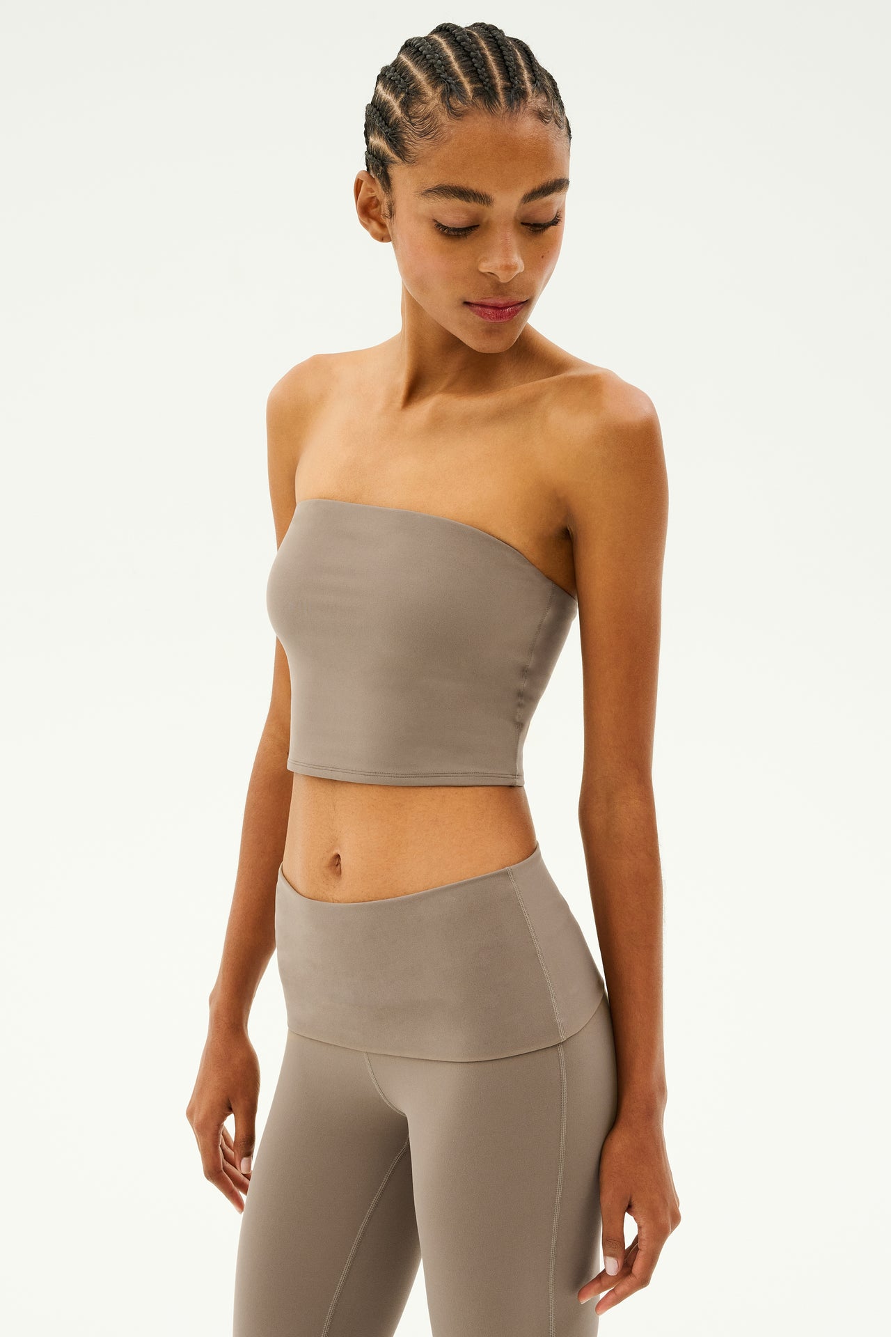 A person wearing a Hazel Airweight Crop Bandeau in Lentil by SPLITS59 and matching Airweight leggings, looking down.