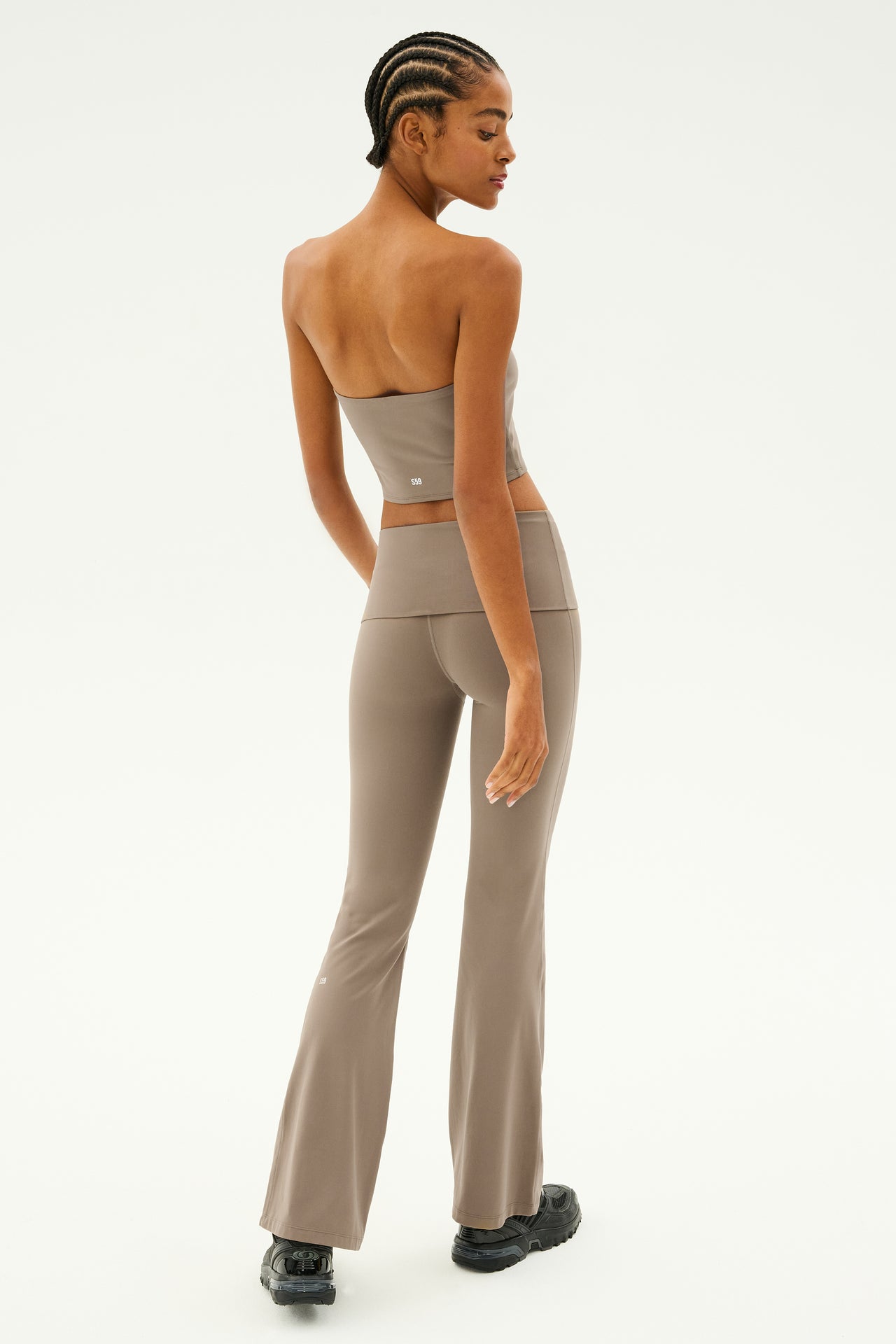 A person is wearing the Raquel Airweight Foldover Flare in Lentil by SPLITS59, featuring a strapless gray top and flared leg pants with a chic foldover waist, standing in profile against a plain background.