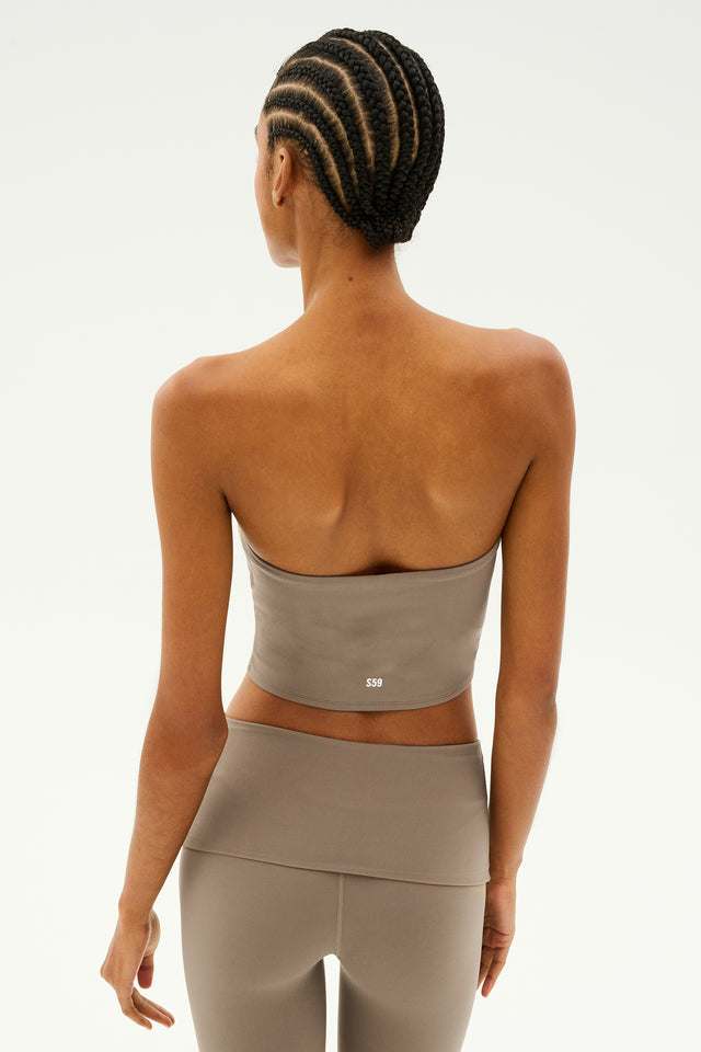 A person with braided hair is seen from the back, wearing a lentil-colored Hazel Airweight Crop Bandeau by SPLITS59 paired with leggings made of stretch fabric, offering both style and support against a plain background.