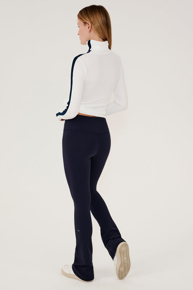 The back view of a woman wearing SPLITS59 Jackson Rib Full Length Turtleneck in White/Indigo yoga track pants.