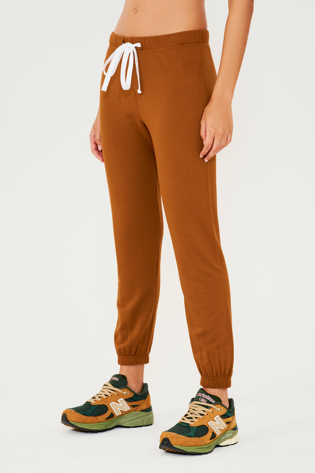 Full front view of woman wearing dark orange sweatpant jogger with white drawstring  paired with dark green, orange and light green shoes
