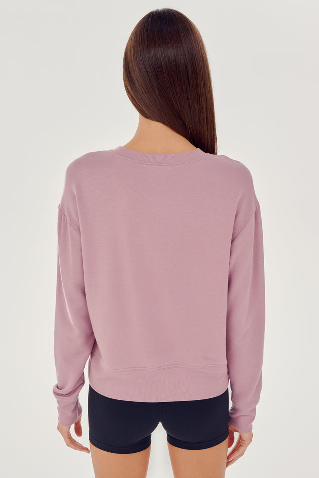 Back view of woman with dark brown hair wearing a light pink crewneck sweatshirt and black shorts 