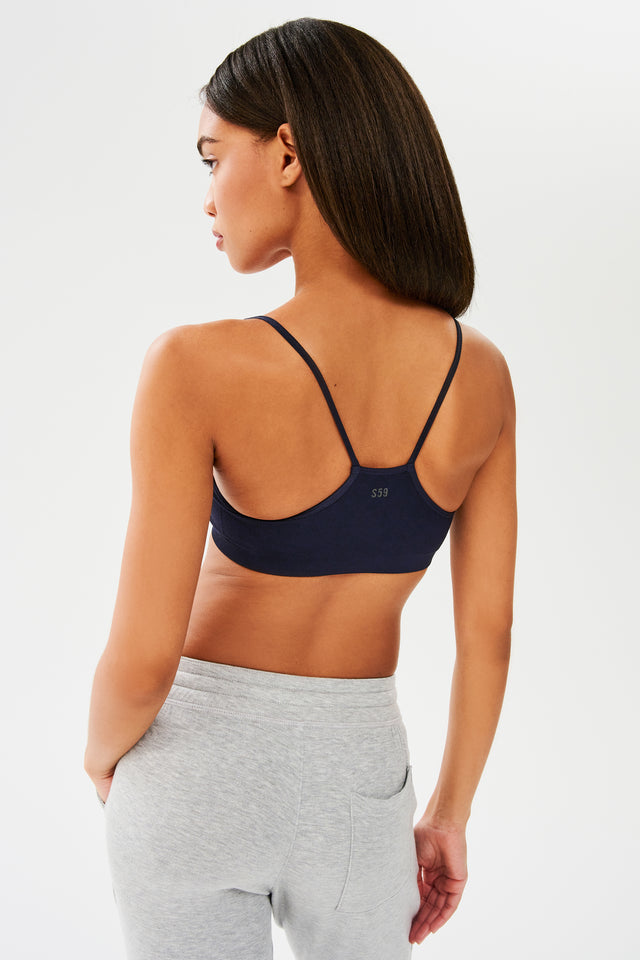 The back view of a woman wearing a SPLITS59 Loren Seamless Bra in Indigo and grey sweatpants.