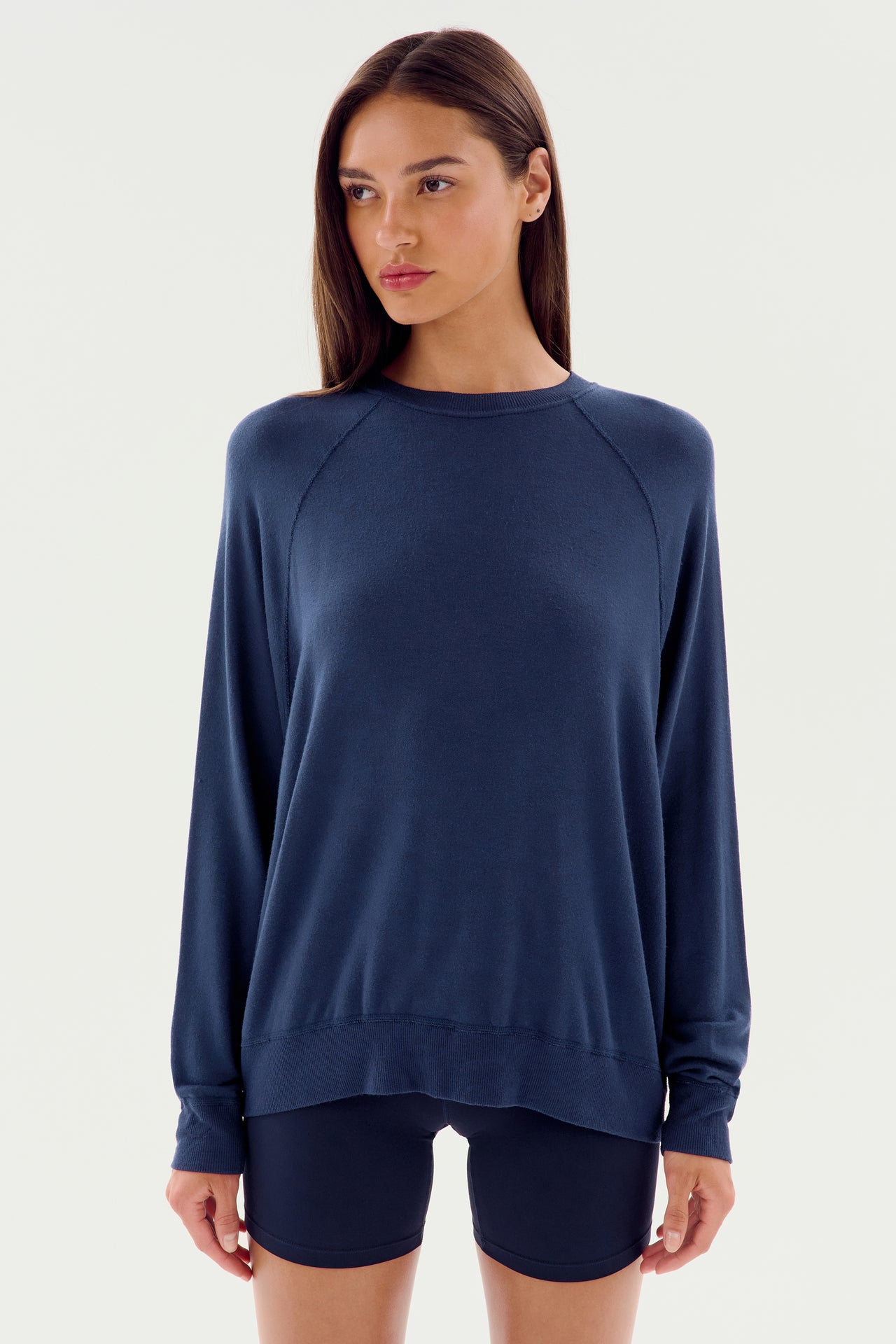 A person wearing the Andie Fleece Sweatshirt - Indigo by SPLITS59 and black shorts stands against a plain white background.