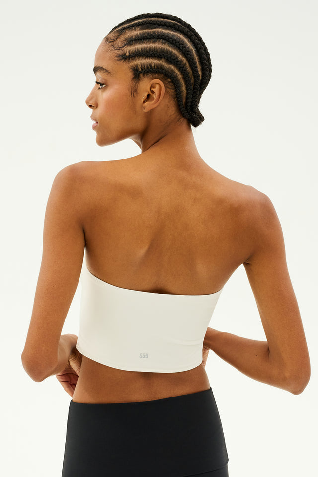 A person with braided hair wears a white Hazel Airweight Crop Bandeau by SPLITS59 and black pants made from stretch fabric, facing away.