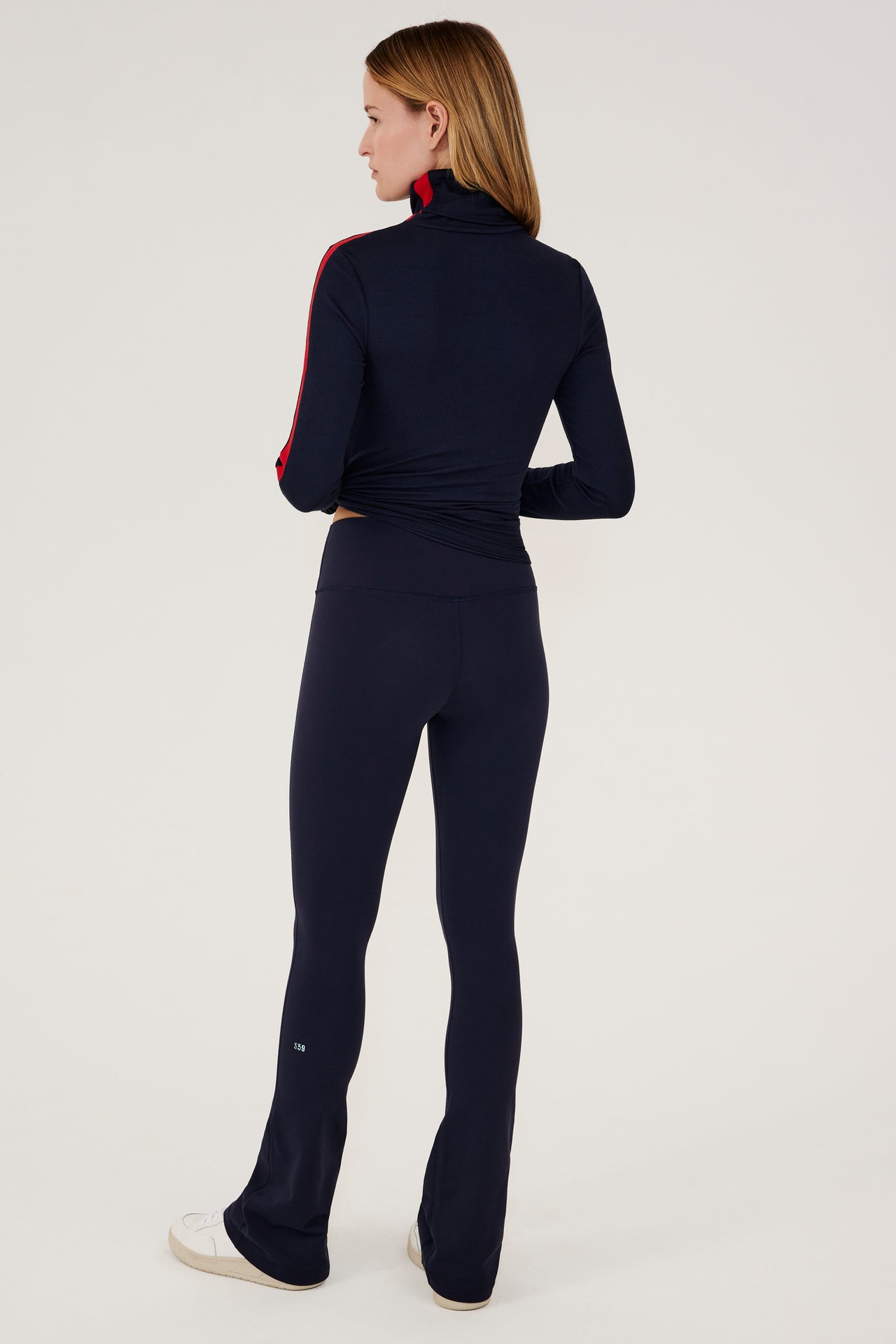The back view of a woman wearing a SPLITS59 Jackson Rib Full Length Turtleneck in Indigo/Pirate Red tracksuit.