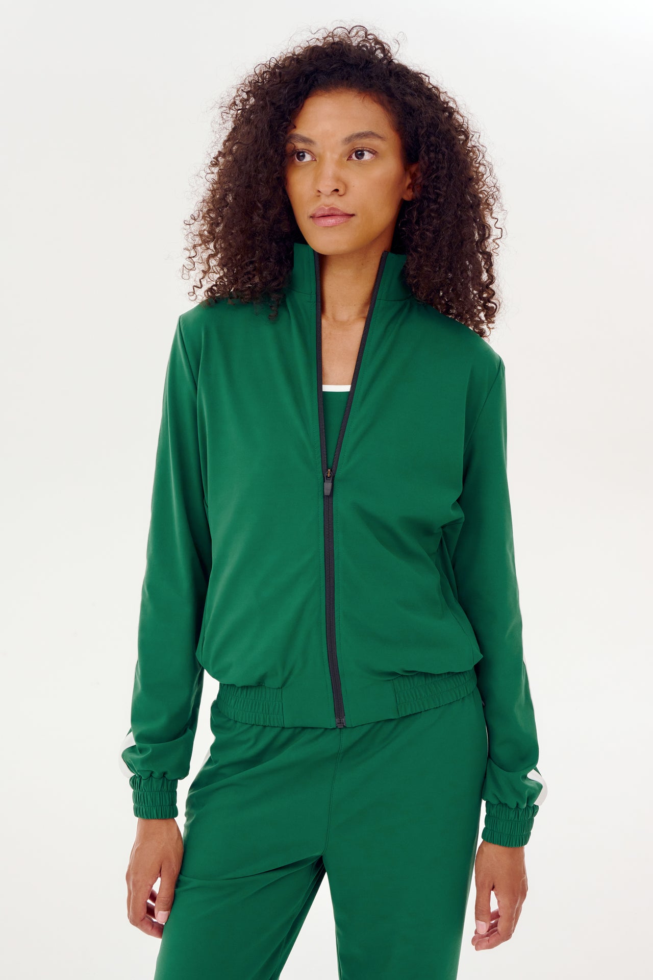 A woman warming up in a green Max Rigor track jacket and pants by SPLITS59.