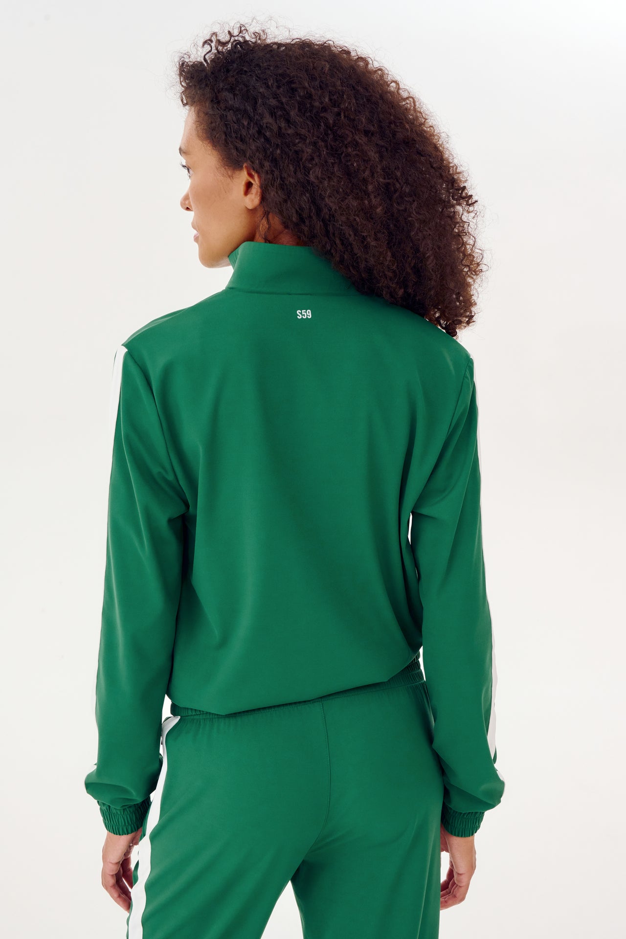 The back view of a woman warming up in a SPLITS59 Max Rigor Track Jacket in Arugula/White.
