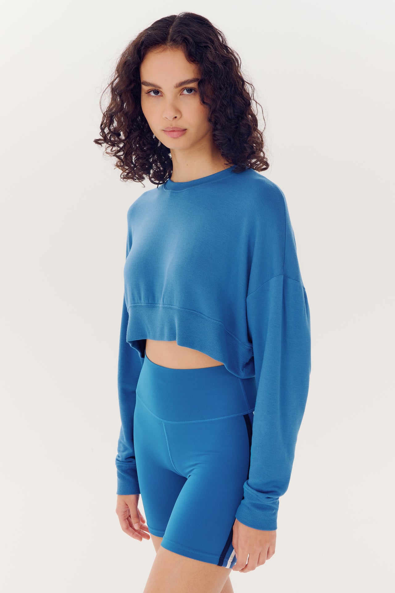 Woman posing in a Noah Fleece Crop Sweatshirt - Stone Blue and matching shorts made from modal spandex blend, by SPLITS59, against a white background.