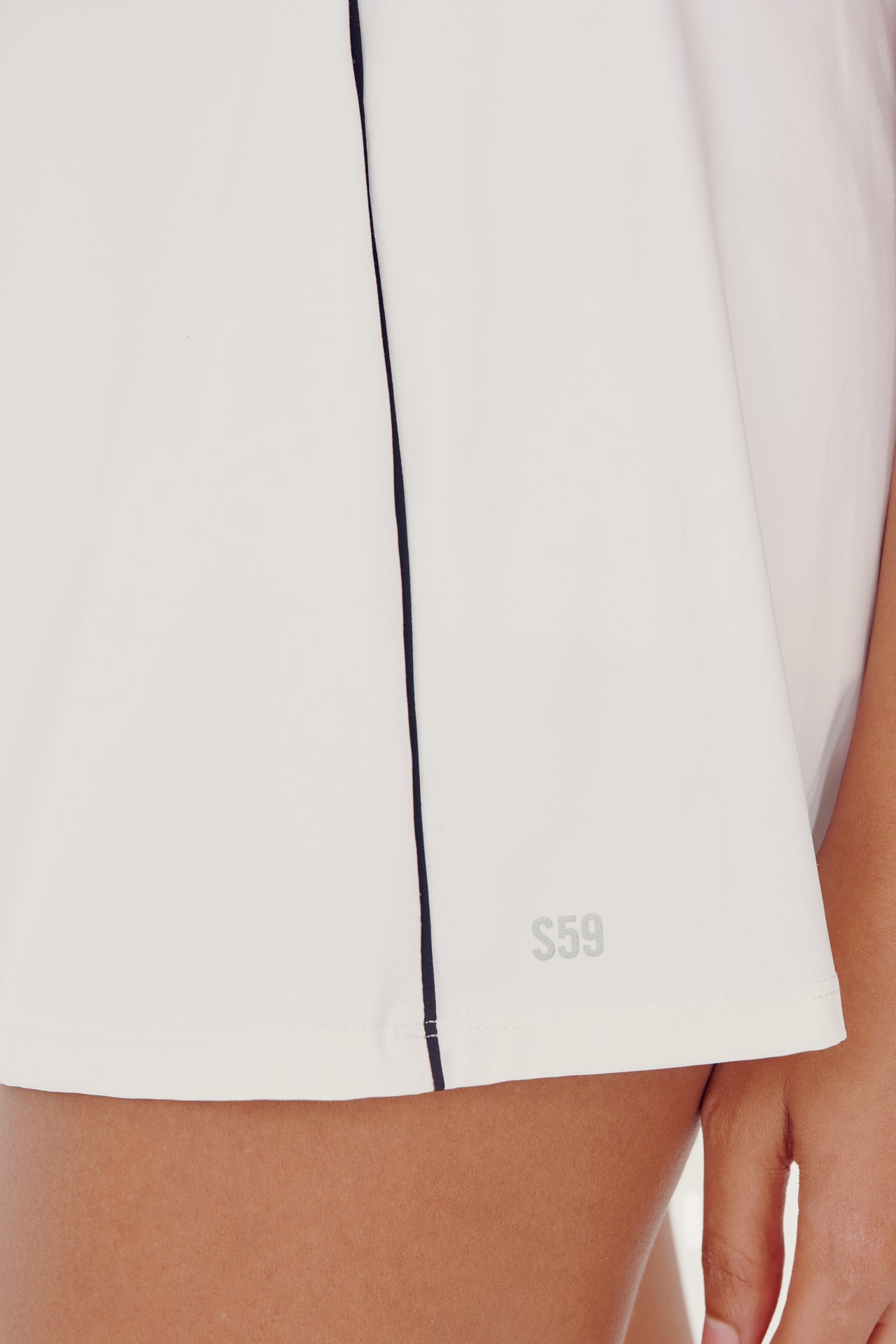 Close-up of a SPLITS59 Venus High Waist Rigor Skort w/Piping - White with a black side seam and the initials 