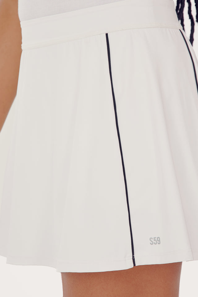 Close-up view of a SPLITS59 Venus High Waist Rigor Skort w/Piping - White with a black vertical stripe on the side, worn by a person with braided hair partially visible.