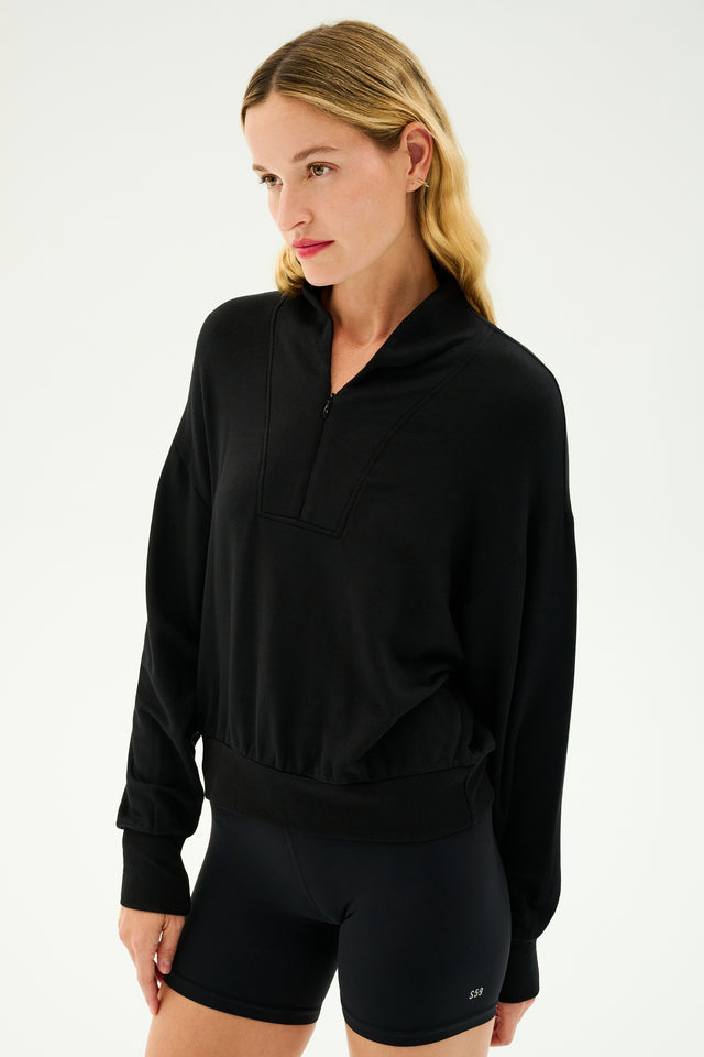 A woman wearing the Birdie Fleece Half Zip in black from SPLITS59, made of stretch modal fabric ideal for winter workouts, stands against a plain background.