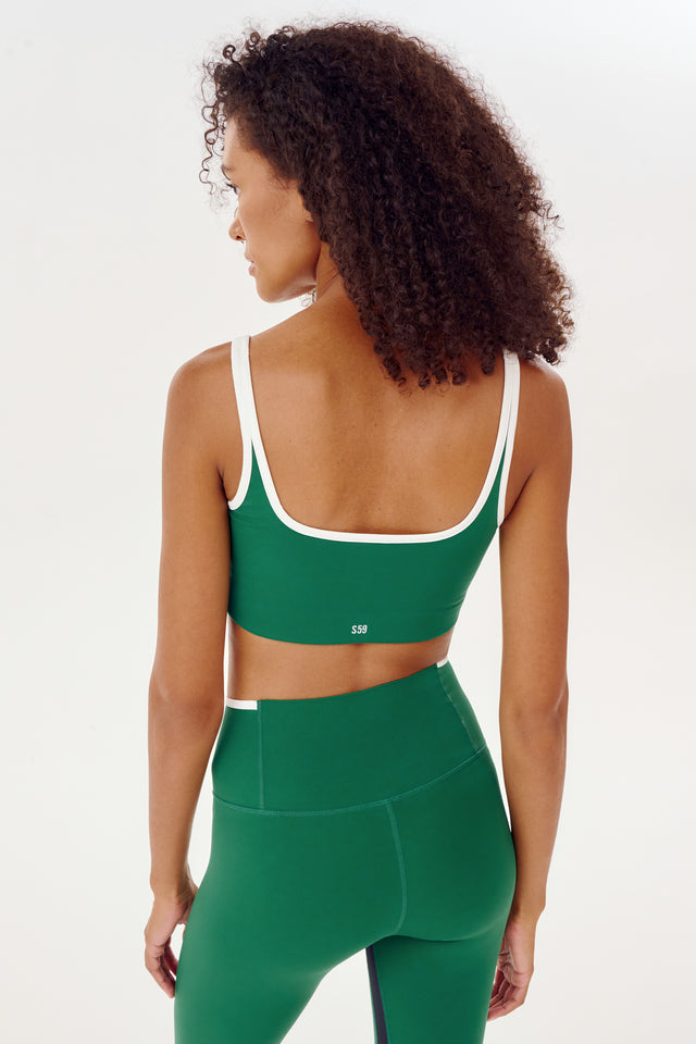 The back view of a woman wearing a SPLITS59 Cait Rigor Bra in Arugula/White and high waist legging.
