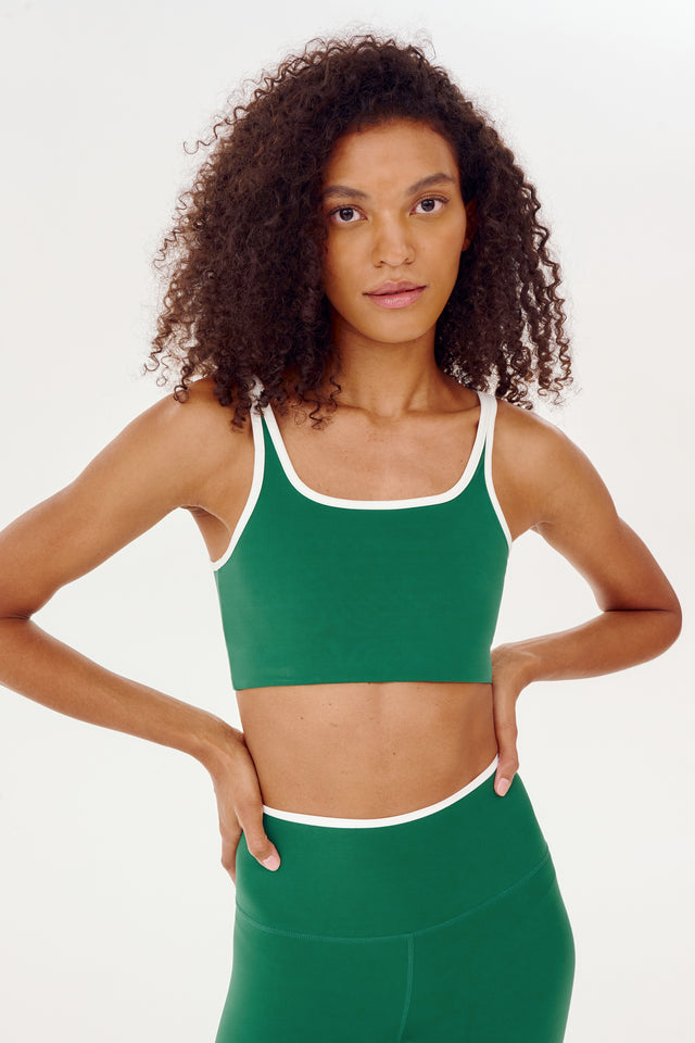 A woman wearing a SPLITS59 Cait Rigor Bra in Arugula/White made from high performance fabric and white high waist leggings.