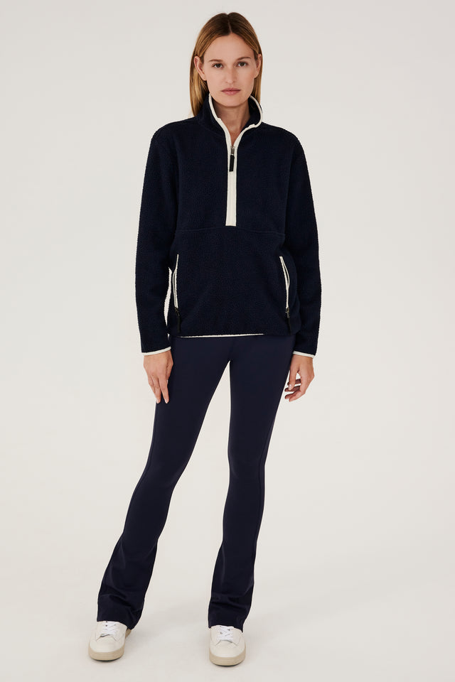 A woman wearing a Libby Sherpa Half Zip in Indigo/Creme and leggings for winter workouts by SPLITS59.