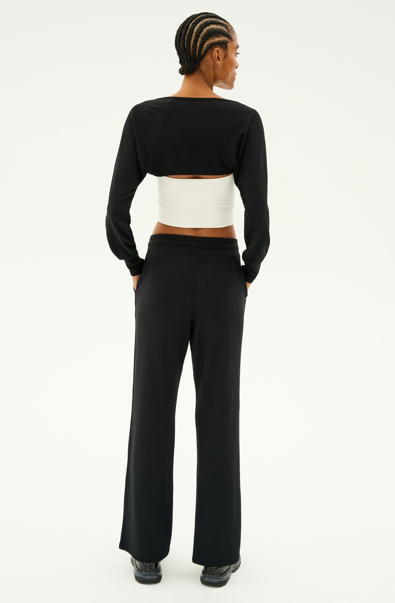 A person is wearing the SPLITS59 Raven Fleece Full Length Sweatpant in black, featuring a white band at the waist, standing with hands in pockets and facing away, exuding the refined elegance of ultra-luxe fleece.