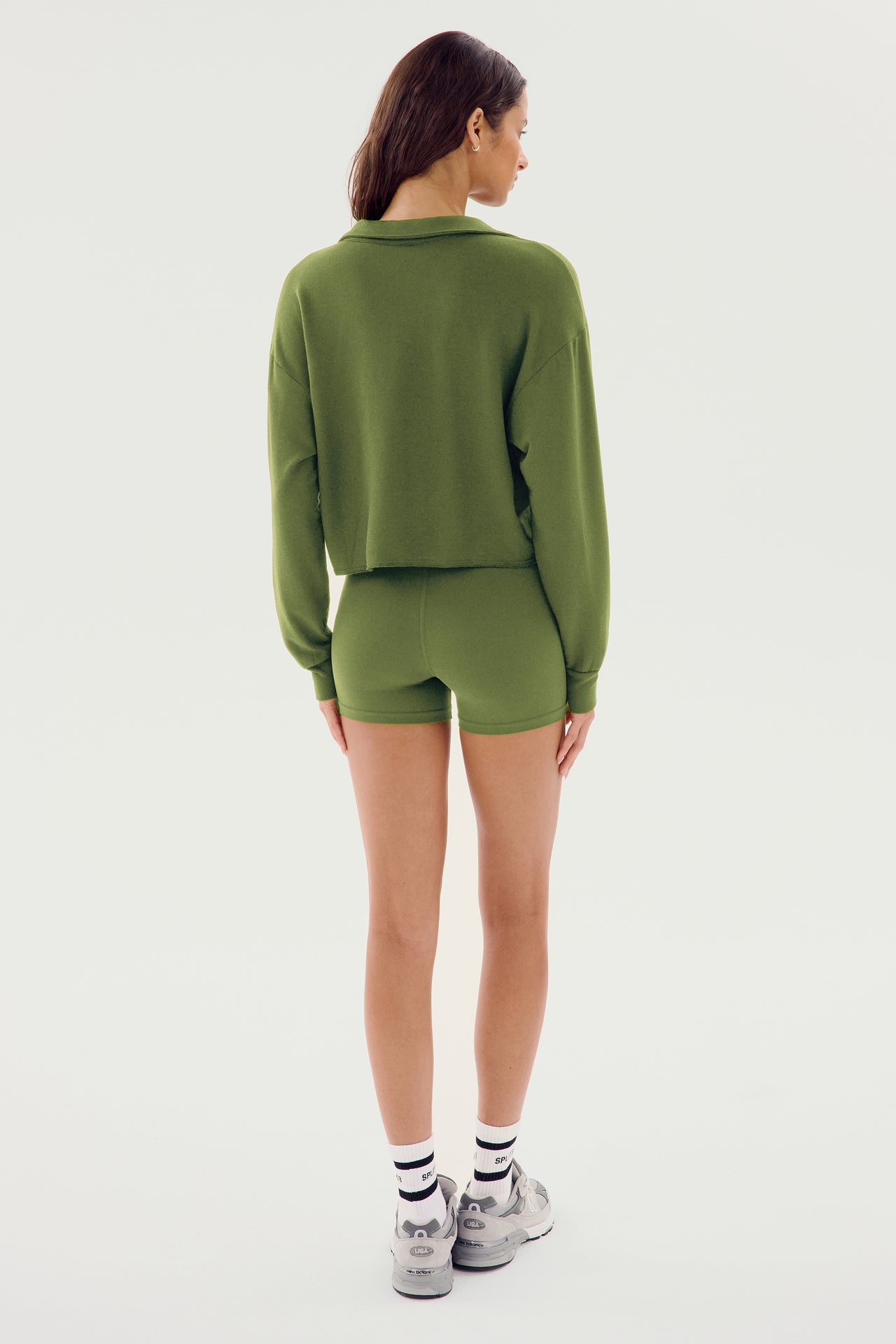 A person wearing an SPLITS59 Joan Fleece Polo Sweatshirt in Olive green and matching spandex shorts, seen from the back, standing against a white background.