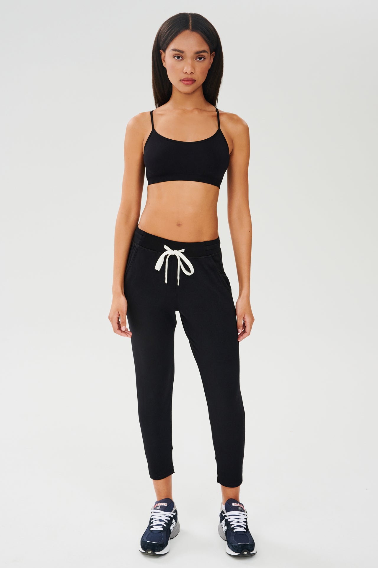 A woman wearing black joggers and a white Splits59 Loren Seamless Bra - Black top.