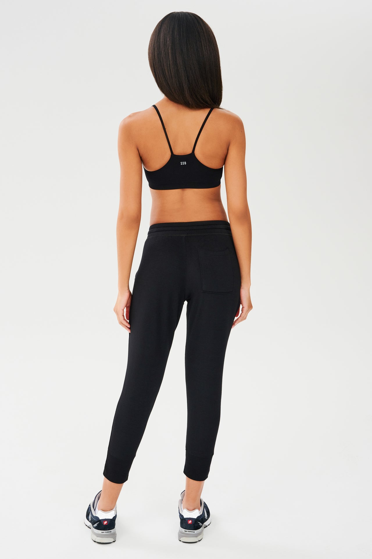 The back view of a woman wearing black, chafe-free fabric leggings and a Splits59 Loren Seamless Bra - Black at the gym.