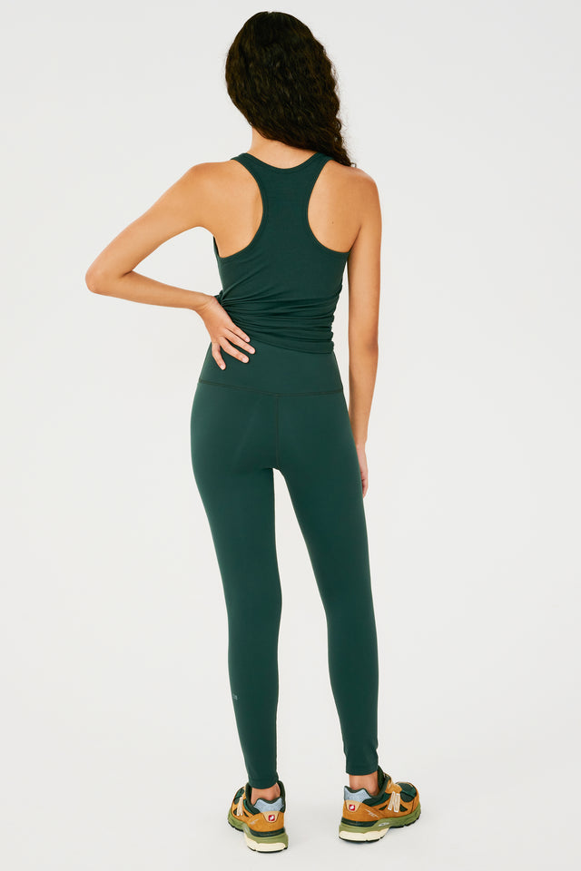 Full back view of girl wearing a dark green tank top tied in a knot at the waist and dark green leggings with multi colored shoes