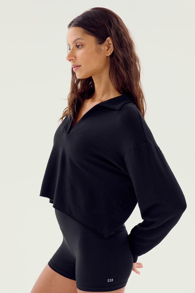 A person is standing in a side profile pose wearing the Joan Fleece Polo Sweatshirt by SPLITS59, matched with black shorts. The outfit is made of soft modal fabric with added spandex for comfort, set against a plain background.