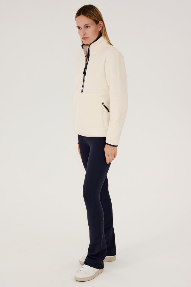 A woman wearing a white Libby Sherpa half-zip jacket and black leggings, perfect for layering during winter workouts from SPLITS59.