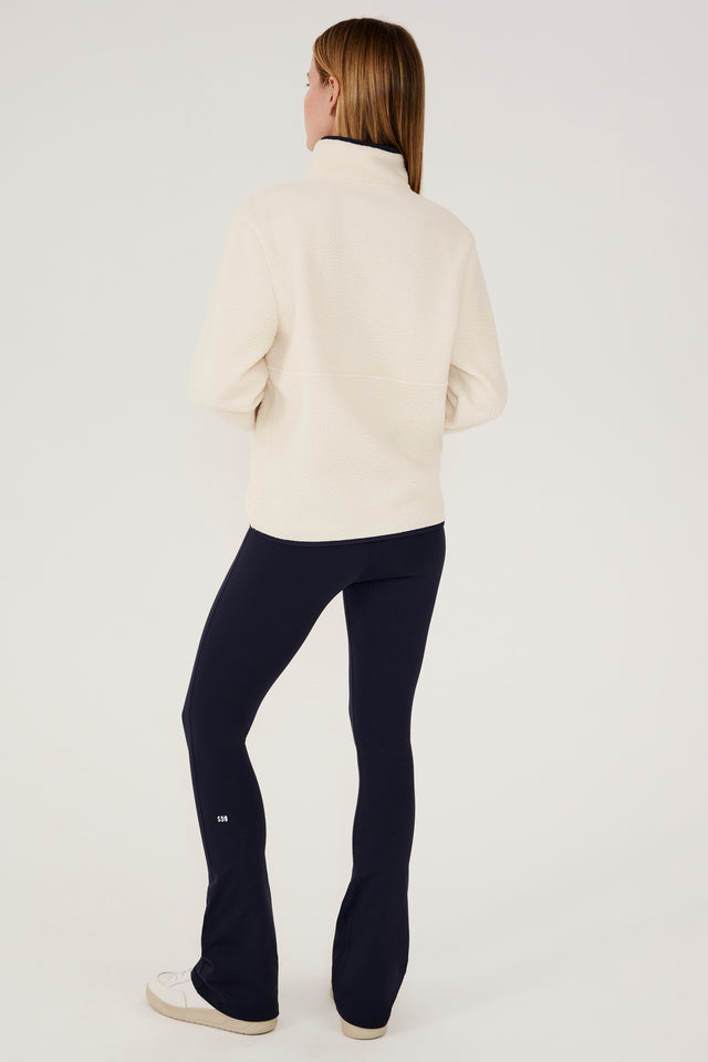 The back view of a woman wearing a white SPLITS59 Libby Sherpa half-zip jacket and black leggings, perfect for layering during winter workouts.